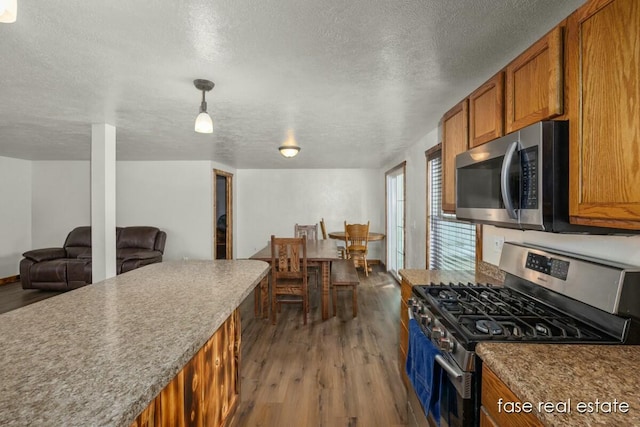 kitchen featuring a textured ceiling, stainless steel appliances, wood finished floors, hanging light fixtures, and brown cabinetry