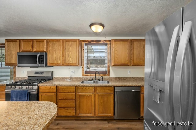 kitchen with brown cabinets, appliances with stainless steel finishes, dark wood-style flooring, and a sink