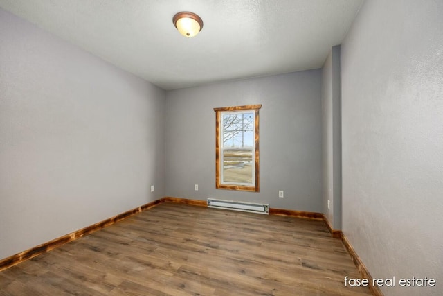 unfurnished room featuring a baseboard radiator, wood finished floors, and baseboards