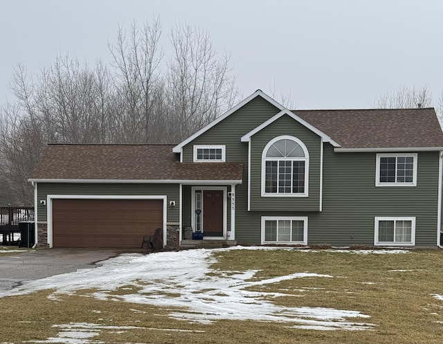 split level home featuring a garage, roof with shingles, and driveway