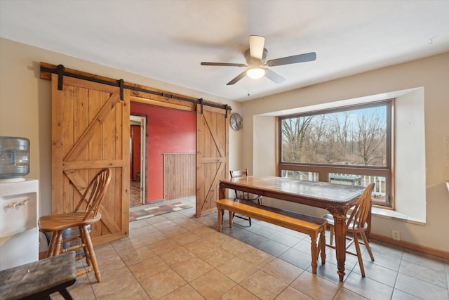 dining room featuring light tile patterned floors, a barn door, a ceiling fan, and baseboards