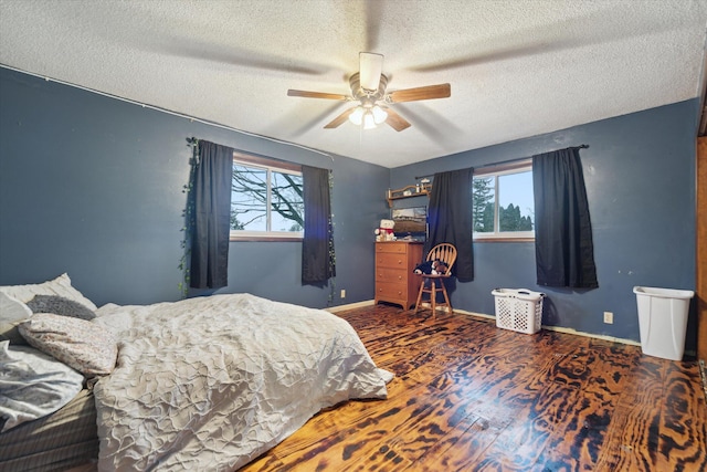 bedroom featuring multiple windows, a textured ceiling, baseboards, and wood finished floors