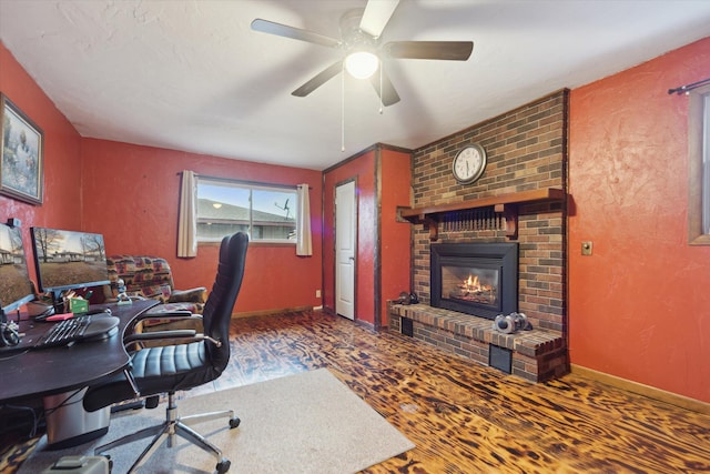 office space with a brick fireplace, ceiling fan, baseboards, and wood finished floors