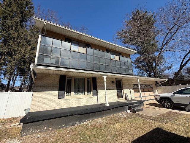 view of front facade with a garage, brick siding, covered porch, and fence