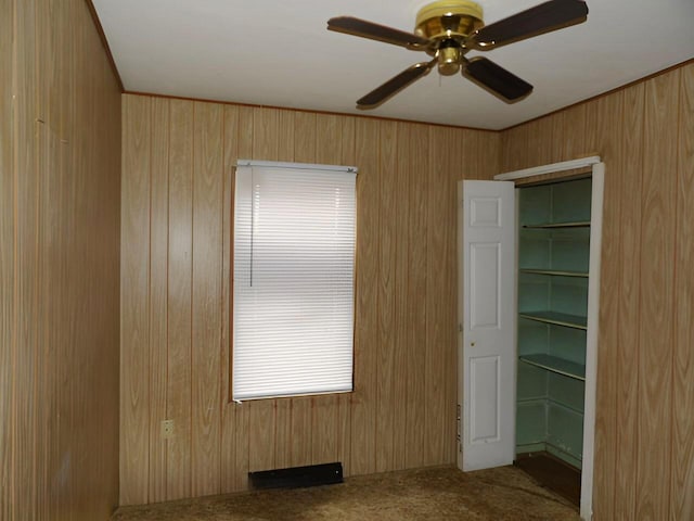 carpeted spare room with a ceiling fan and wooden walls