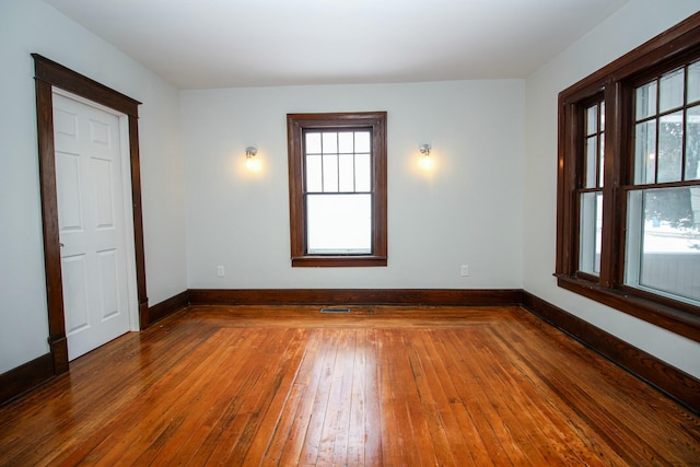 spare room with plenty of natural light, wood-type flooring, visible vents, and baseboards