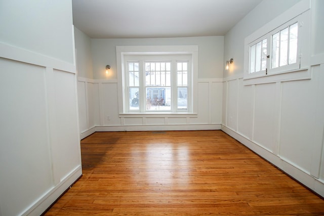 unfurnished room with a wainscoted wall, a decorative wall, and light wood-style floors