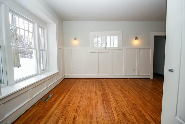 empty room featuring a wainscoted wall, visible vents, a decorative wall, and wood finished floors