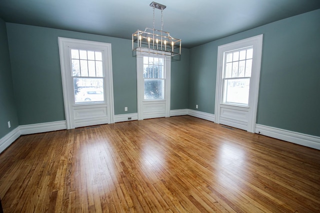 unfurnished room featuring a chandelier, hardwood / wood-style floors, and baseboards