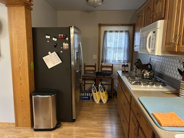 kitchen with white microwave, light wood-type flooring, stainless steel fridge, and tasteful backsplash