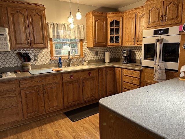 kitchen featuring white appliances, a sink, light wood-style floors, brown cabinets, and glass insert cabinets