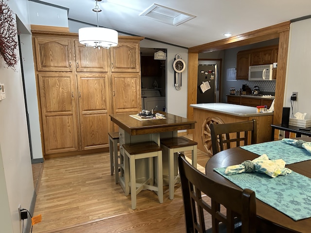 kitchen featuring washer / dryer, white microwave, freestanding refrigerator, light wood-style floors, and backsplash