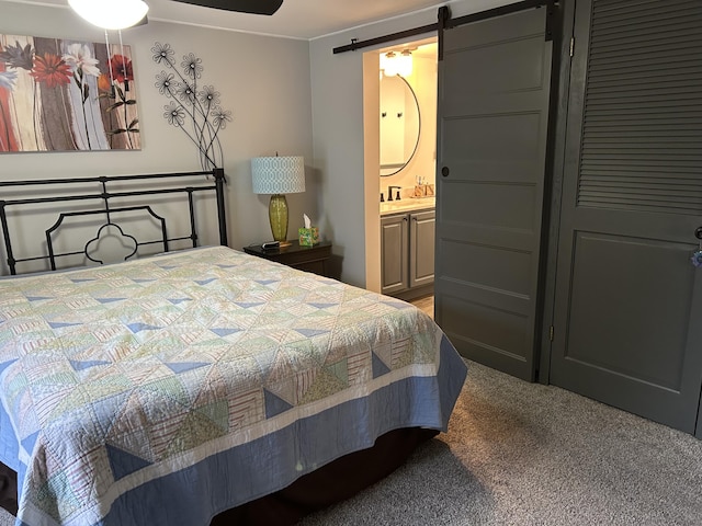 bedroom with light colored carpet, connected bathroom, and a barn door