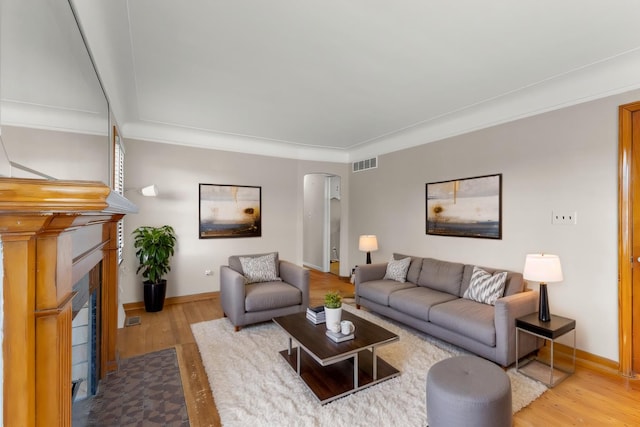 living room with a fireplace with flush hearth, arched walkways, visible vents, and wood finished floors