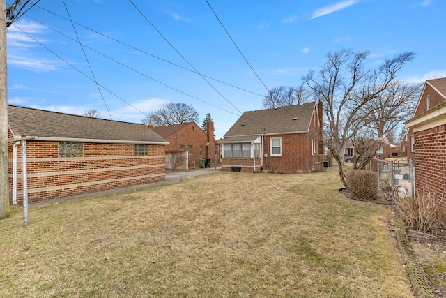 back of house with a shingled roof, a lawn, and brick siding