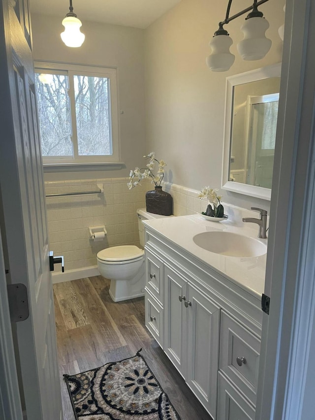 bathroom with toilet, a wainscoted wall, wood finished floors, vanity, and tile walls