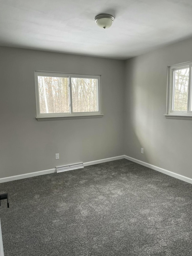 empty room with baseboard heating, dark carpet, and baseboards