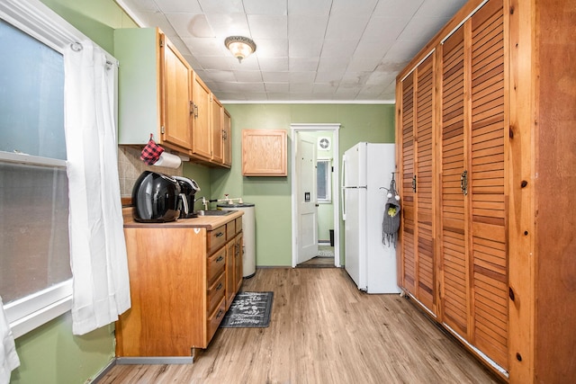 kitchen with light wood finished floors, tasteful backsplash, light countertops, freestanding refrigerator, and washer / dryer