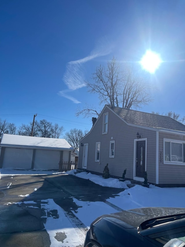 view of snow covered exterior featuring an outbuilding, roof with shingles, and a garage