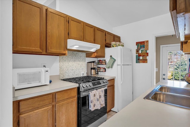 kitchen featuring under cabinet range hood, tasteful backsplash, white appliances, light countertops, and vaulted ceiling