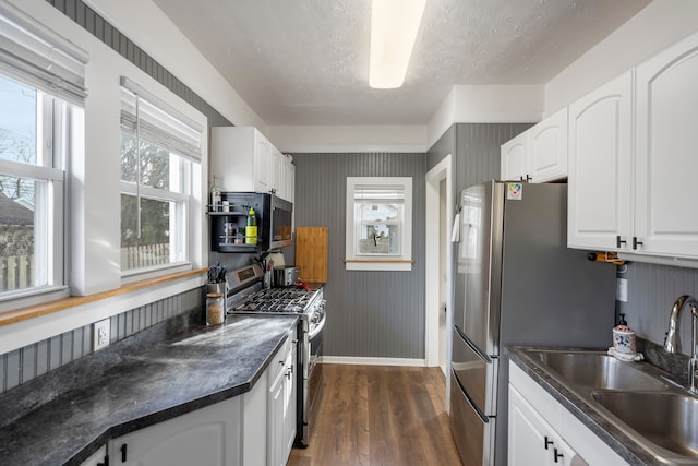 kitchen with a sink, white cabinets, stainless steel range with gas cooktop, dark wood-style floors, and dark countertops