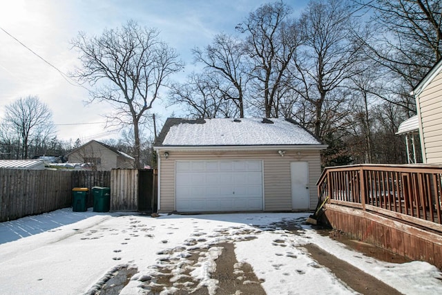 snow covered garage featuring a detached garage and fence