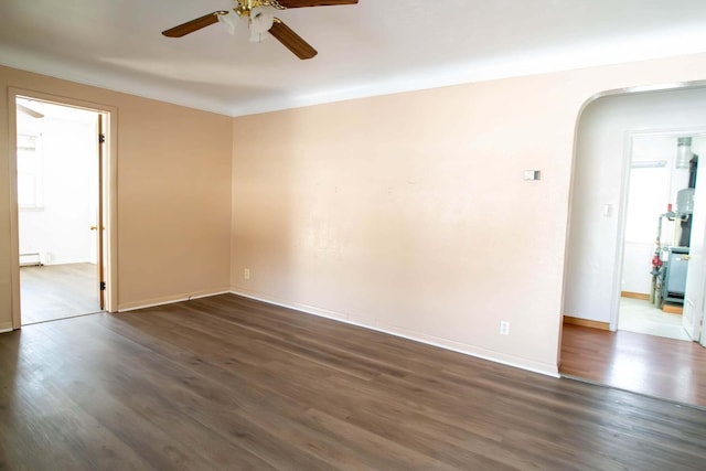 spare room featuring dark wood-style floors, arched walkways, a baseboard radiator, ceiling fan, and baseboards