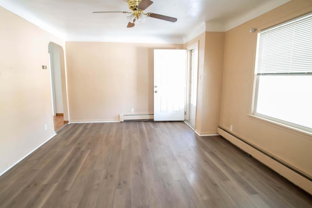 empty room with a baseboard heating unit, arched walkways, and wood finished floors