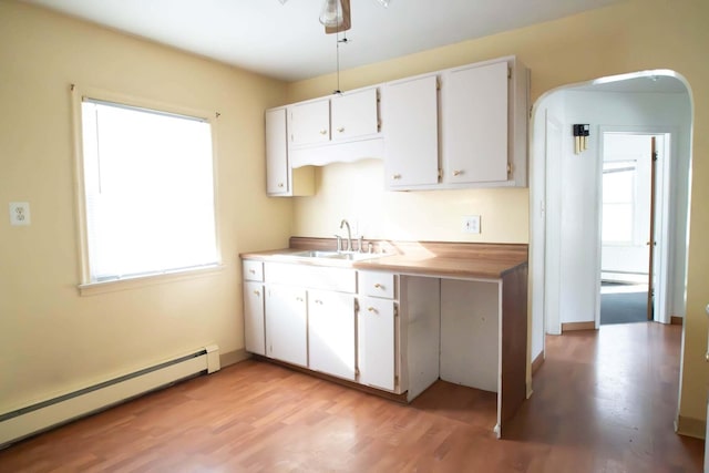 kitchen featuring a healthy amount of sunlight, a baseboard heating unit, arched walkways, and a sink