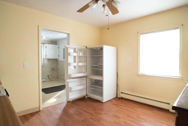 unfurnished bedroom with light wood-style flooring, a baseboard heating unit, a ceiling fan, and ensuite bathroom