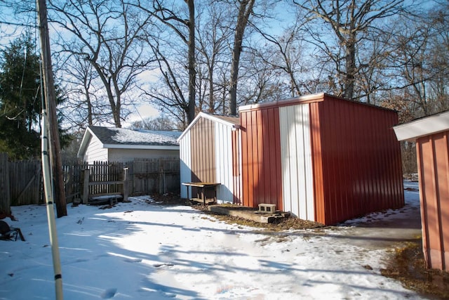 snow covered structure with a shed, an outdoor structure, and fence