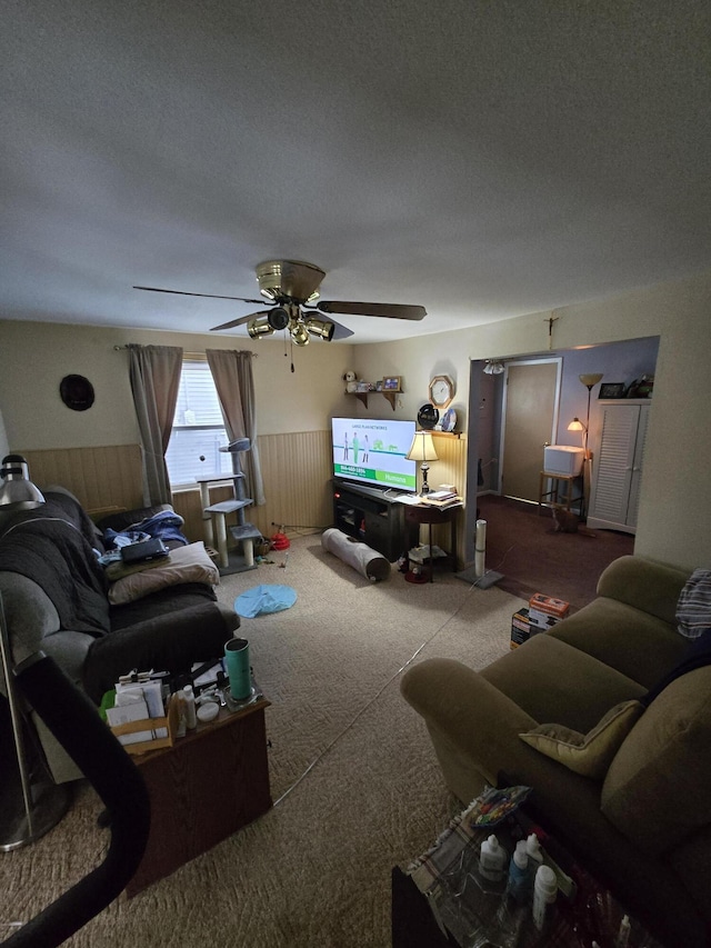 carpeted living room with a textured ceiling, wainscoting, and a ceiling fan