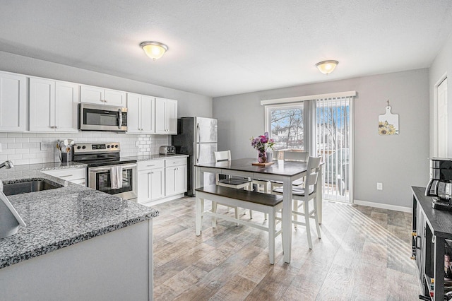 kitchen featuring light wood finished floors, tasteful backsplash, dark stone countertops, stainless steel appliances, and a sink