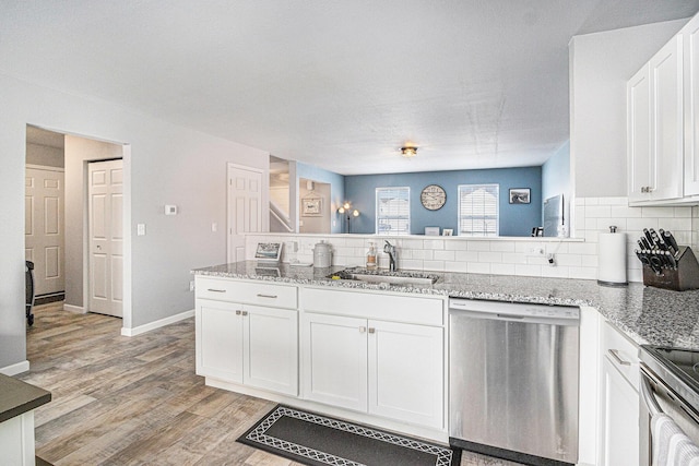 kitchen featuring light wood finished floors, stainless steel appliances, white cabinets, a sink, and a peninsula