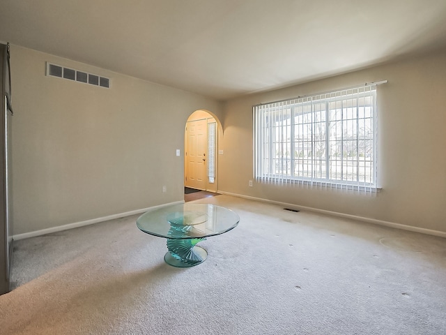 spare room featuring arched walkways, visible vents, and carpet