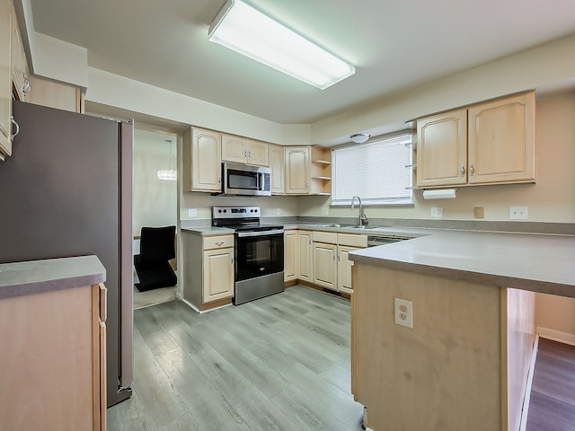 kitchen with appliances with stainless steel finishes, a peninsula, light wood-style floors, light brown cabinets, and a sink