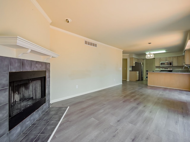 unfurnished living room featuring a tile fireplace, wood finished floors, a sink, visible vents, and crown molding