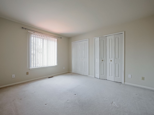 unfurnished bedroom featuring carpet floors, two closets, visible vents, and baseboards