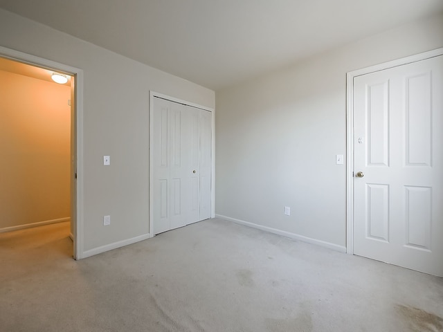 unfurnished bedroom featuring a closet, light carpet, and baseboards