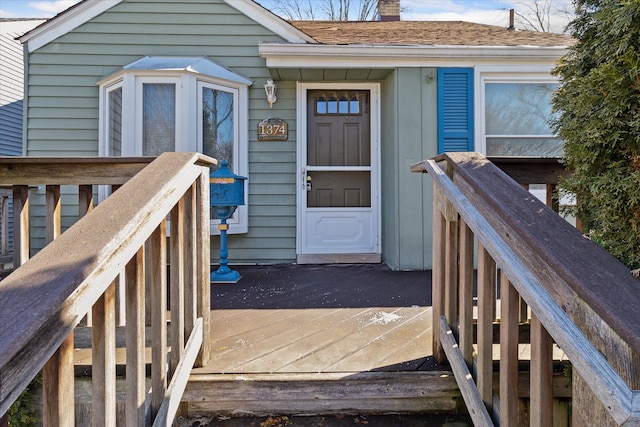 view of exterior entry featuring a shingled roof, a chimney, and a deck