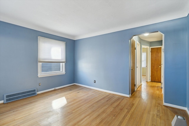 empty room with light wood-type flooring, baseboards, visible vents, and arched walkways