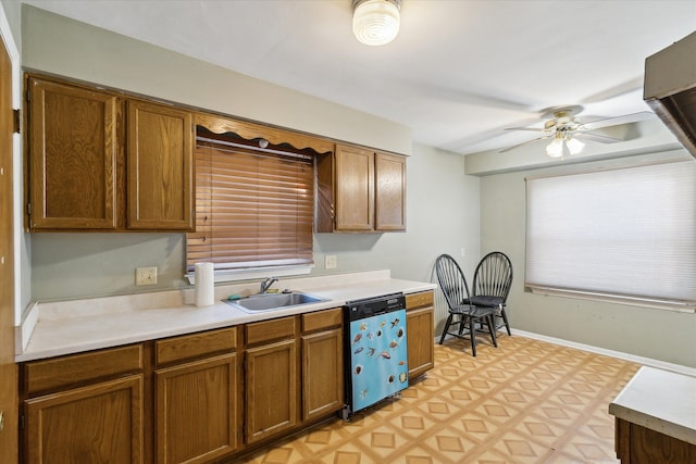 kitchen with light floors, light countertops, brown cabinetry, a sink, and dishwashing machine