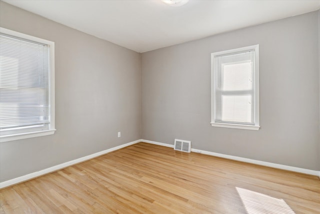 unfurnished room with light wood-style floors, visible vents, plenty of natural light, and baseboards