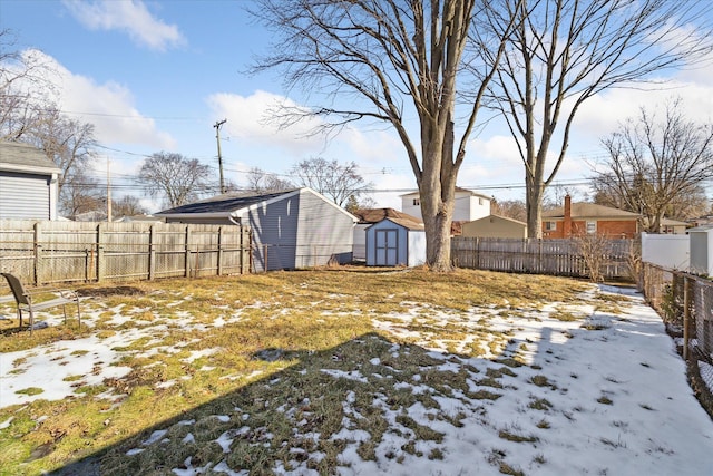 snowy yard featuring an outbuilding, a fenced backyard, and a shed