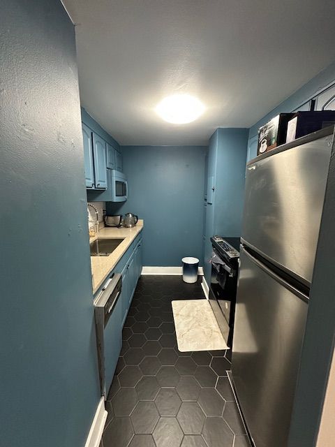 kitchen with electric range oven, light countertops, blue cabinetry, freestanding refrigerator, and dishwasher