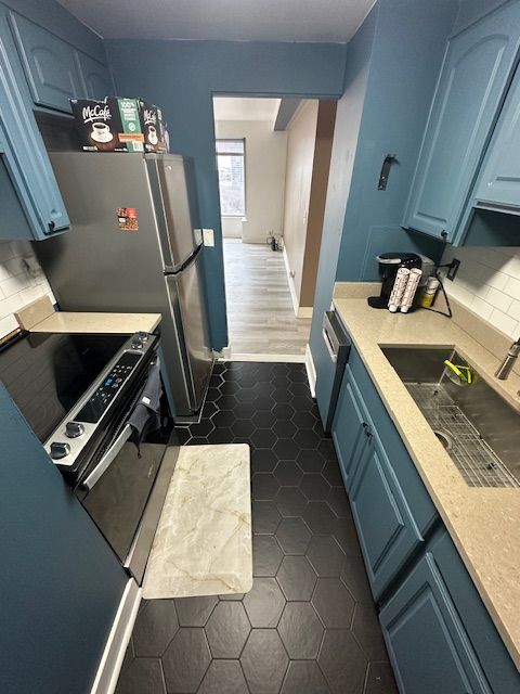 kitchen featuring dark tile patterned flooring, a sink, light countertops, blue cabinetry, and tasteful backsplash