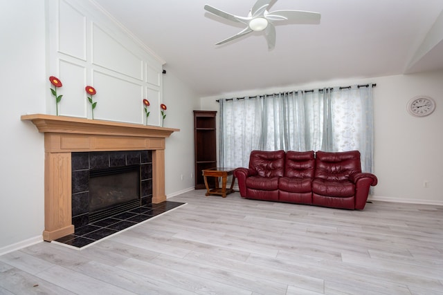 living area featuring light wood-style flooring, vaulted ceiling, ceiling fan, a tile fireplace, and baseboards