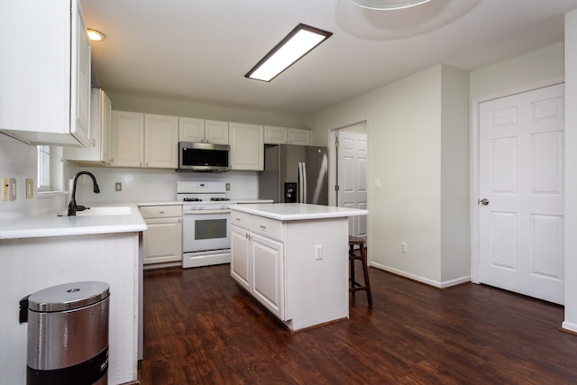 kitchen with light countertops, appliances with stainless steel finishes, white cabinetry, a sink, and a kitchen island