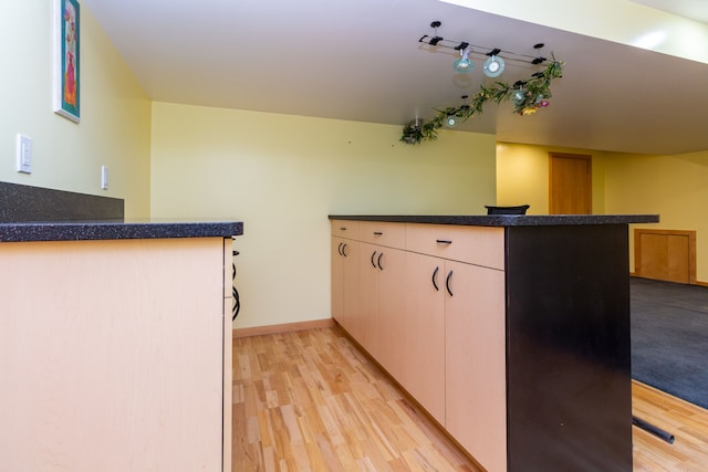 kitchen featuring a peninsula, dark countertops, light wood-style flooring, and baseboards