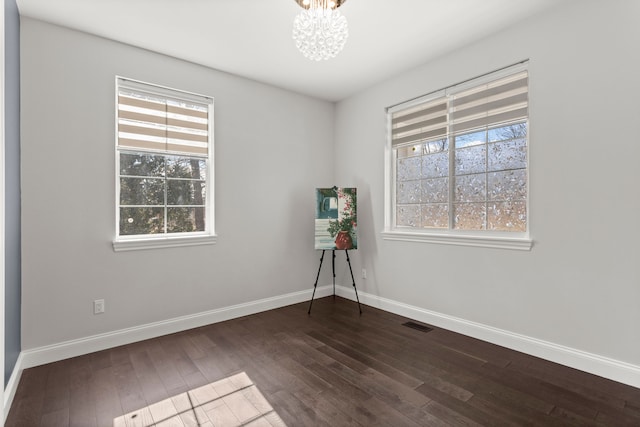 unfurnished room with baseboards, dark wood-type flooring, visible vents, and an inviting chandelier